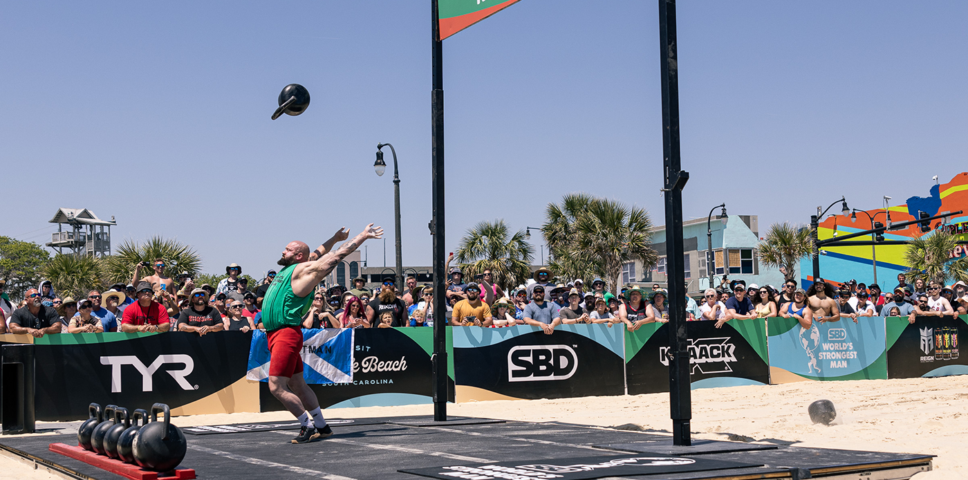 strong looking man tossing a kettelbell over his head