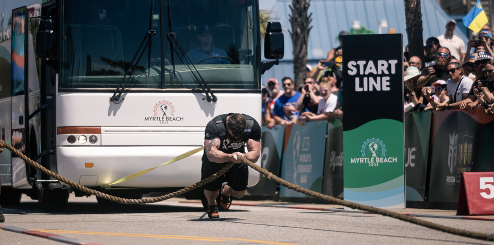 strong man pulling a coach sized bus