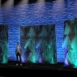 Rendering of a Shell modular scenic wall installed on stage with performers in front under blue and green lighting.