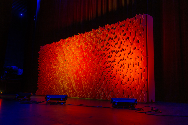 Angled view of a Pixel modular scenic wall installed on a stage and lit in warm red tones.